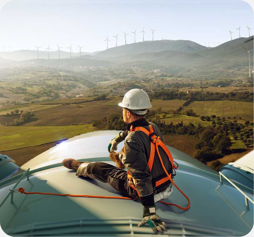 a man wearing a hard hat and safety harness sitting on top of a wind turbine