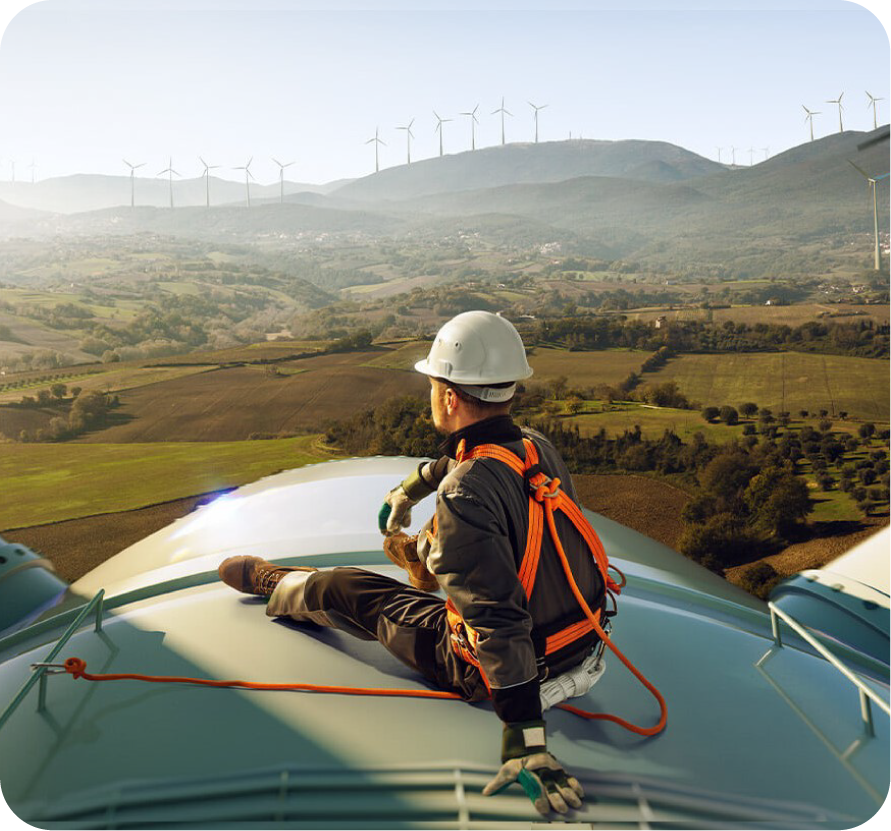 a man wearing a hard hat and safety harness sitting on top of a wind turbine